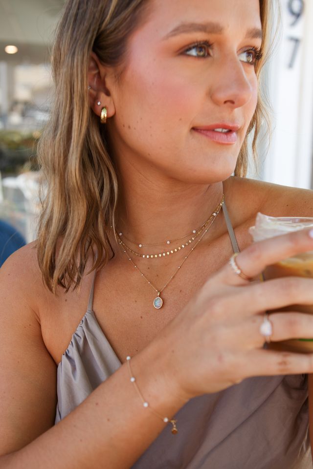 A woman in delicate gold jewelry holding a coffee cup