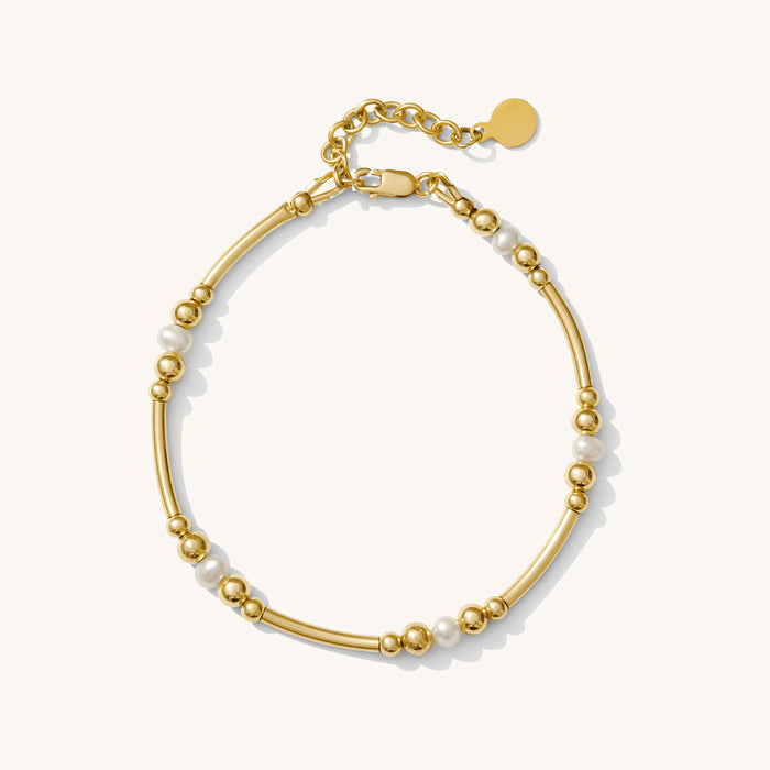 Close up of a gold bracelet with pearl accents on a white background