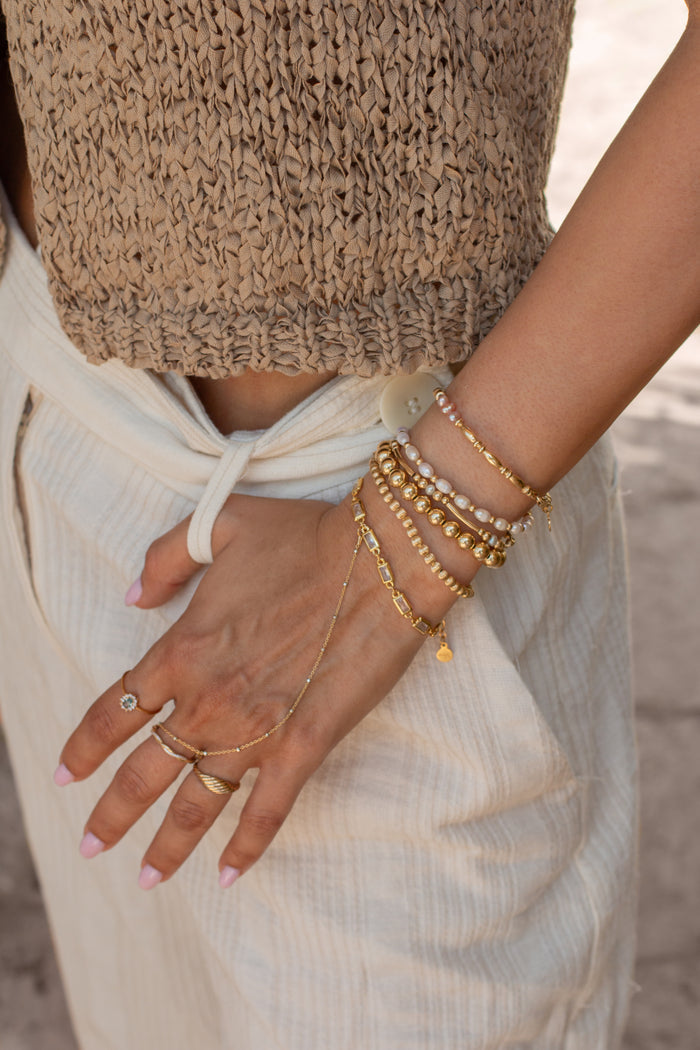 A person wearing a brown top, blue pants, and assorted gold jewelry on a tan background