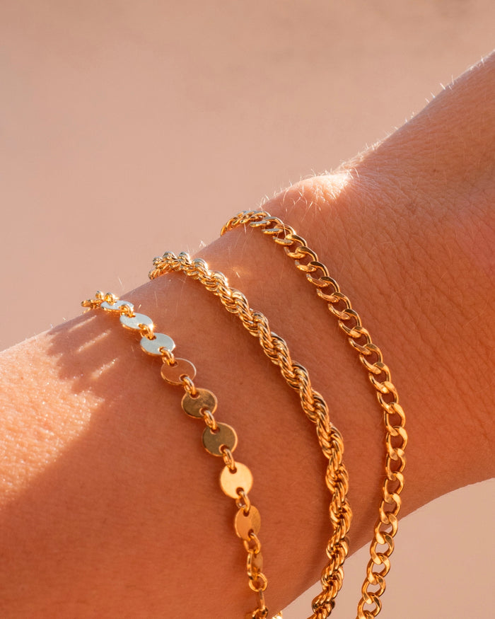 Close up of a wrist with dainty gold bracelets on a pink background