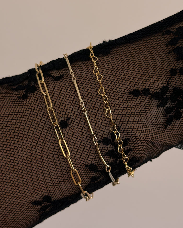 Close up of a wrist with a black lace sleeve and three gold chain bracelets