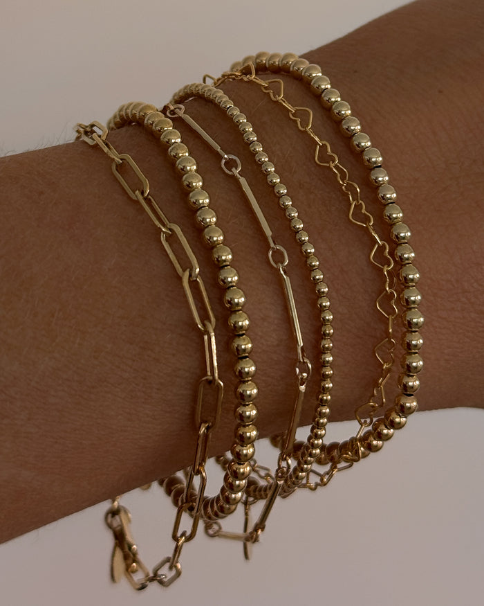 Close up of a wrist with assorted gold bracelets against a white background
