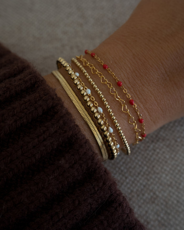 Close up of a wrist with a brown sweater and assorted gold and bead bracelets