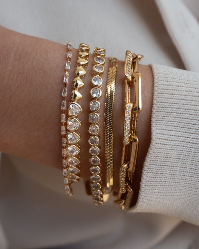 Close up of a wrist in a white sweater with assorted gold bracelets
