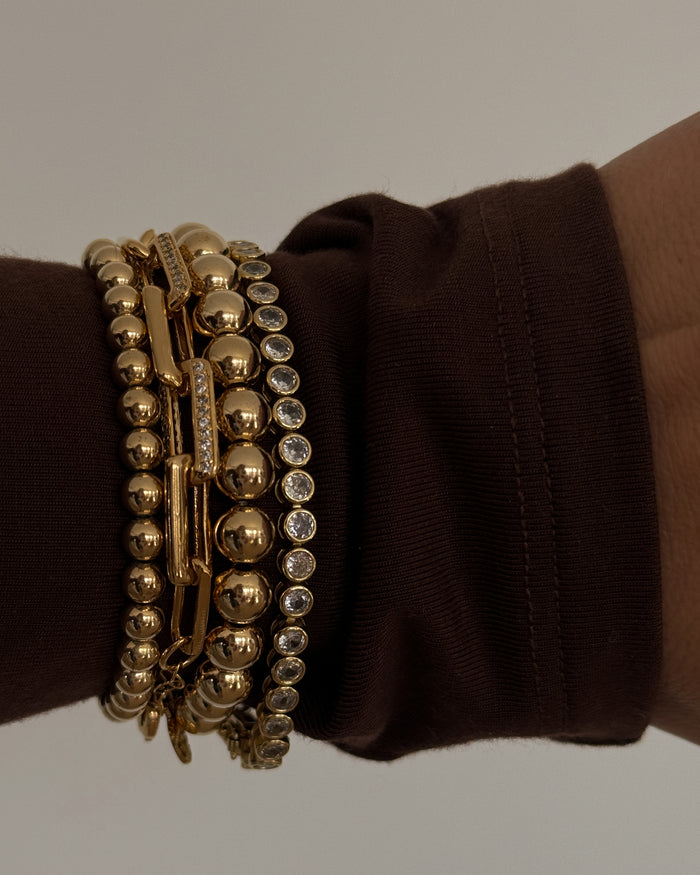 Close up of a wrist in a maroon sweater with gold and stone bracelets