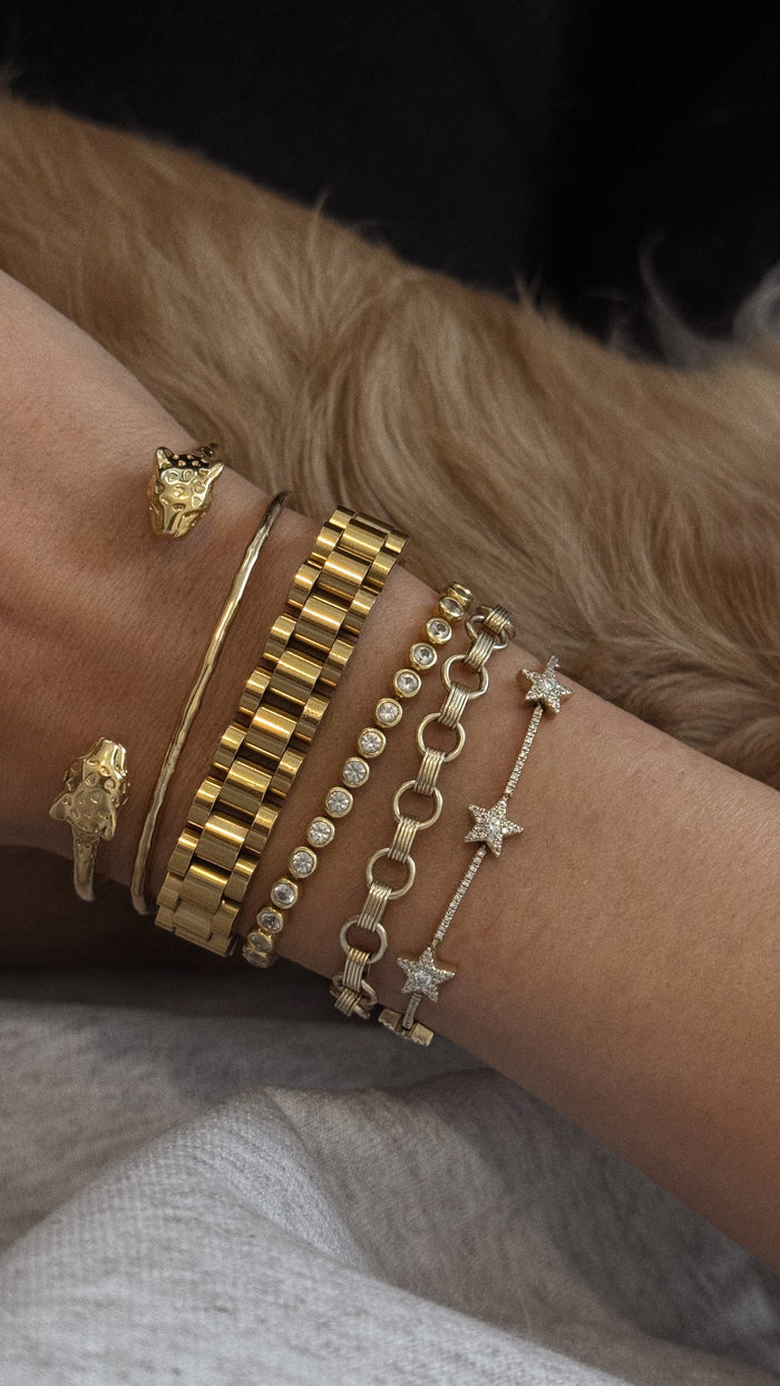 Close up of a wrist with assorted gold and stone bracelets against a brown fur background