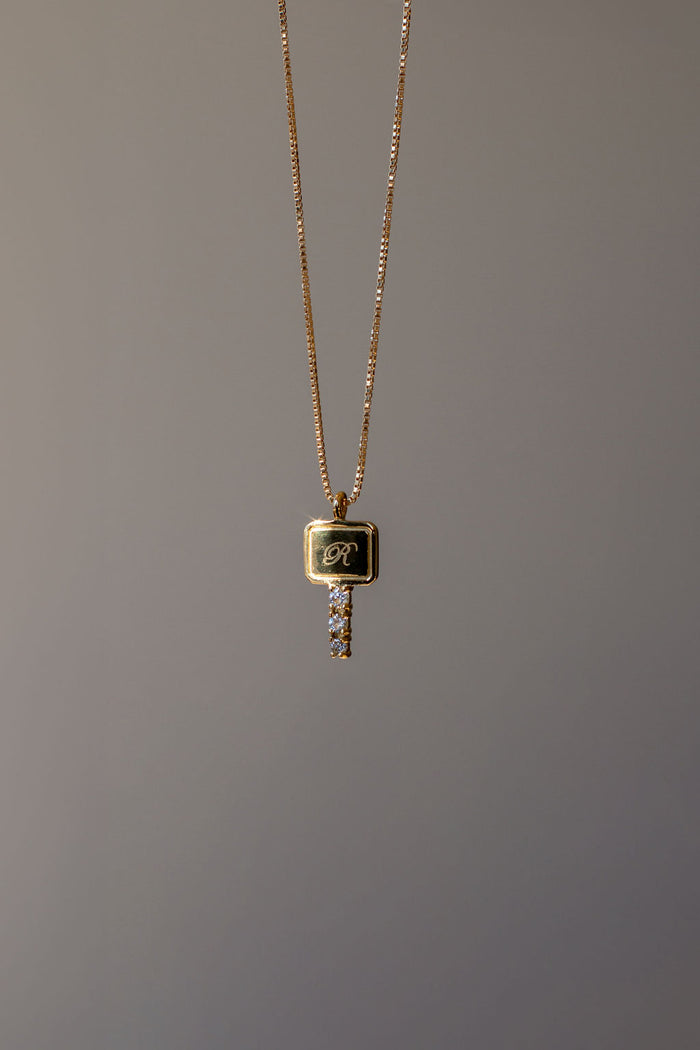A delicate gold chain necklace with a crystal set key pendant