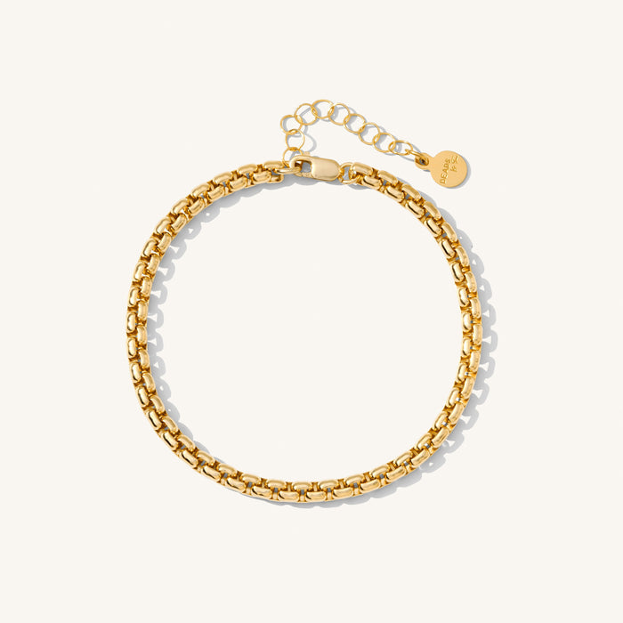 Close up of a gold curb chain bracelet on a white background