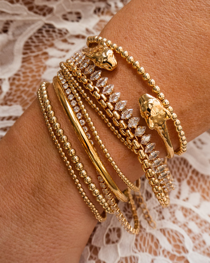 Close up of a wrist with gold and stone bracelets on a lace background