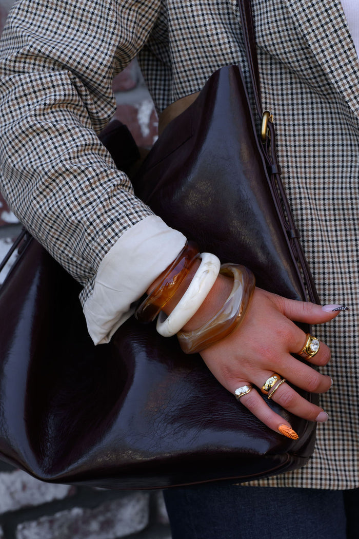 A person in a checkered blazer carrying a brown bag with gold and resin bracelets and rings