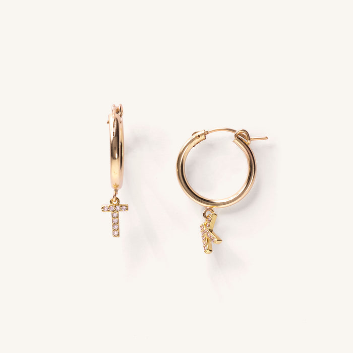 Close up of gold hoops with stone initial charms on a white background