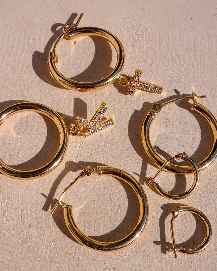 Close-up of multiple pairs of gold hoops with charms on a neutral background