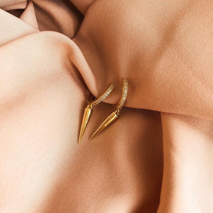 Close up of gold huggies with stones and geometric charms on a neutral cloth background