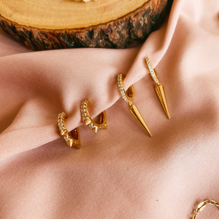 Two pairs of gold hoops with stone accents on a pink cloth background