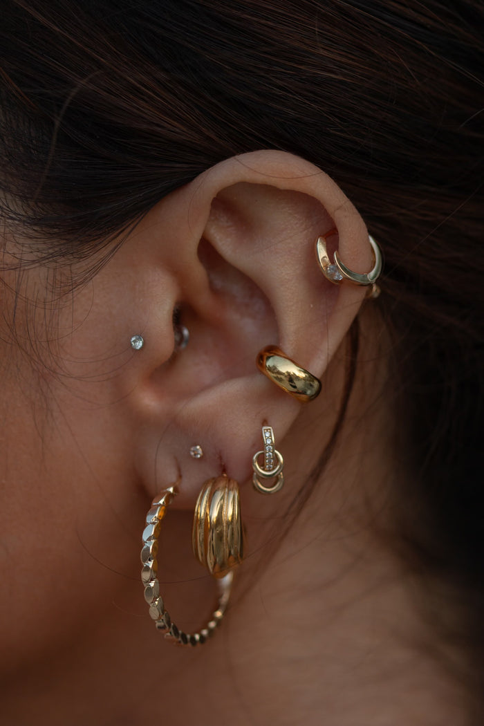 Close-up of an ear with multiple gold and crystal earrings
