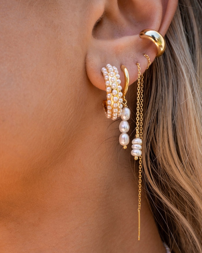 Close-up of an ear with multiple gold and pearl earrings