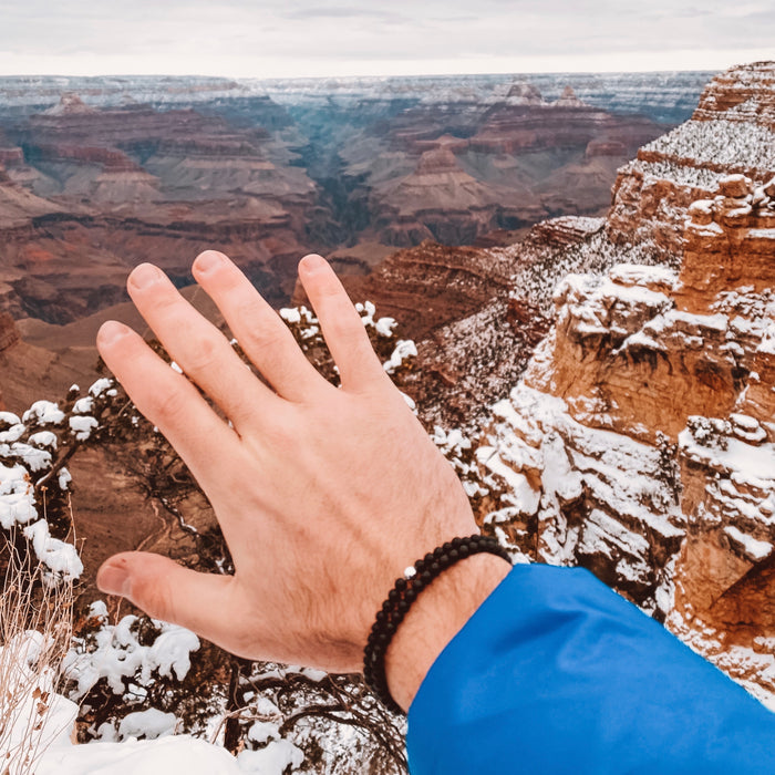 A person's wrist with a blue jacket and black bracelets, with a view of canyons in the background