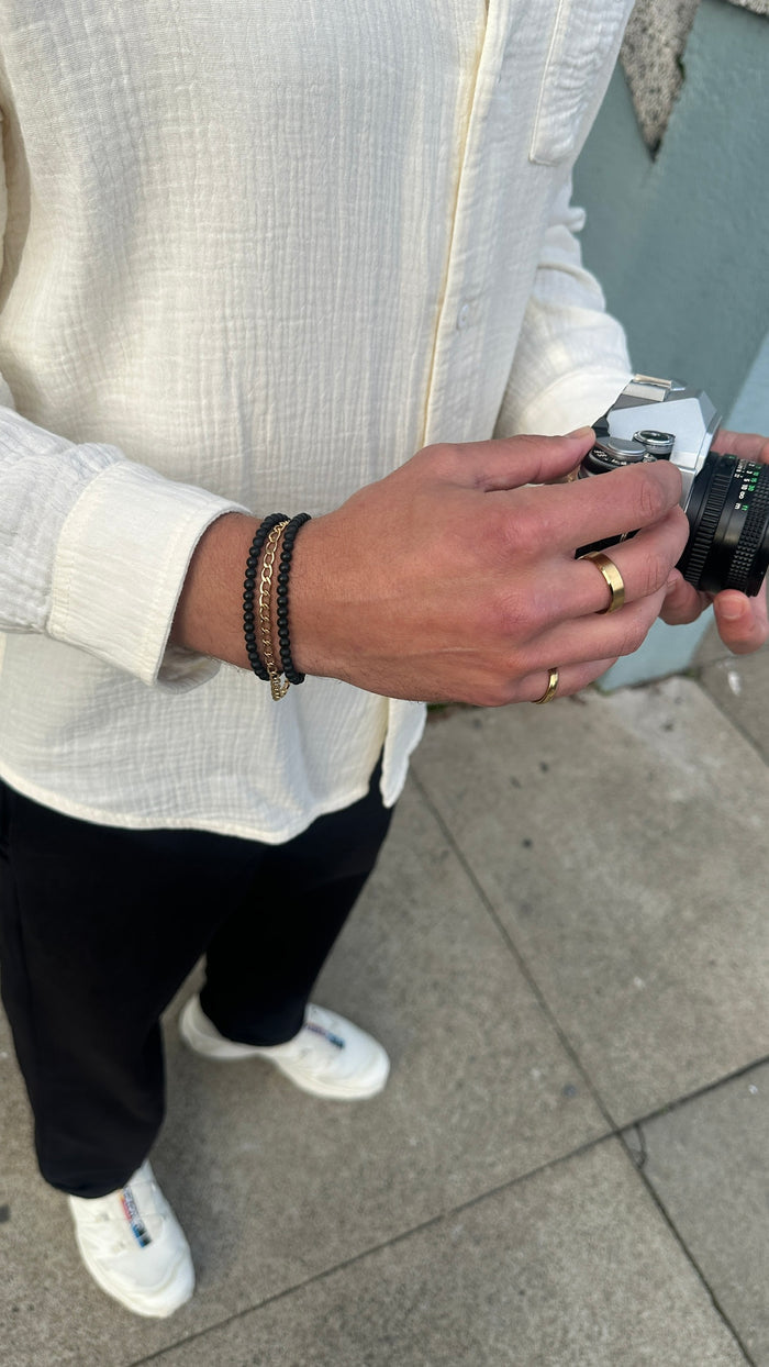 A person wearing a white shirt, black pants, white sneakers, gold rings, and black jewelry standing on a sidewalk
