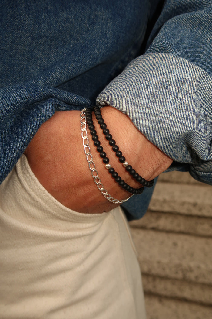 Close up of a person wearing a blue denim jacket and stone bracelets, with their hand tucked into their pocket