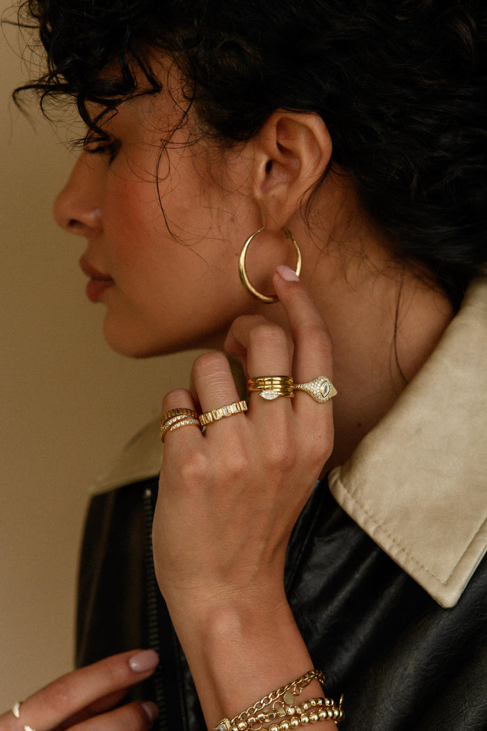 Side shot of a woman wearing a pair of gold hoops, rings, and bracelets
