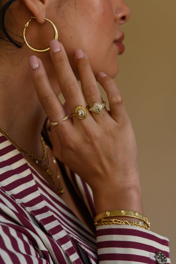 Close up of a woman in a striped shirt wearing gold hoops, rings, necklaces, and bracelets