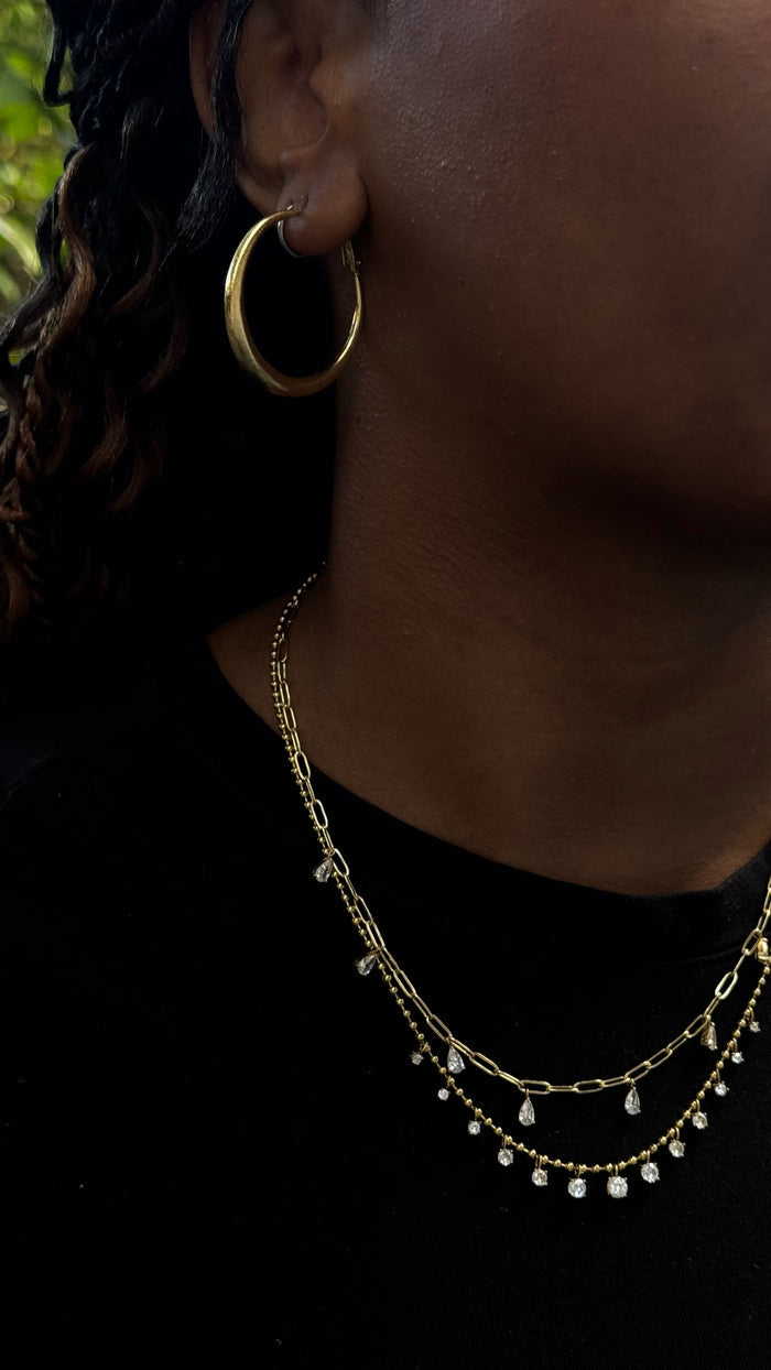 Close up shot of a woman wearing a pair of gold hoops and layered necklaces