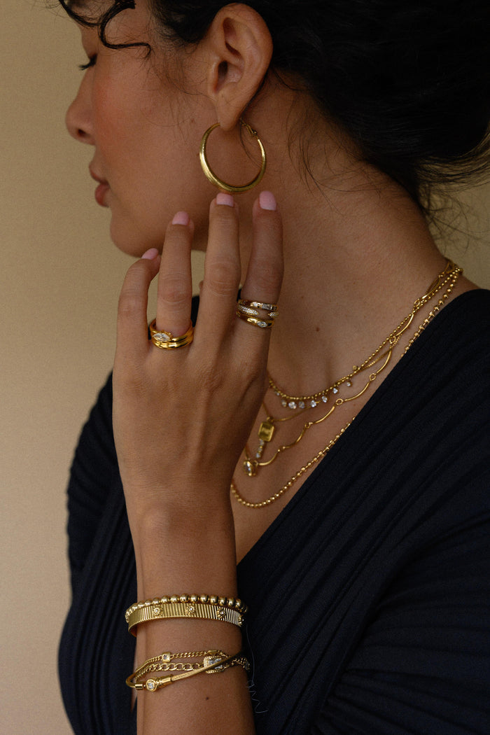 Close up of a woman wearing gold hoops, rings, necklaces, and bracelets