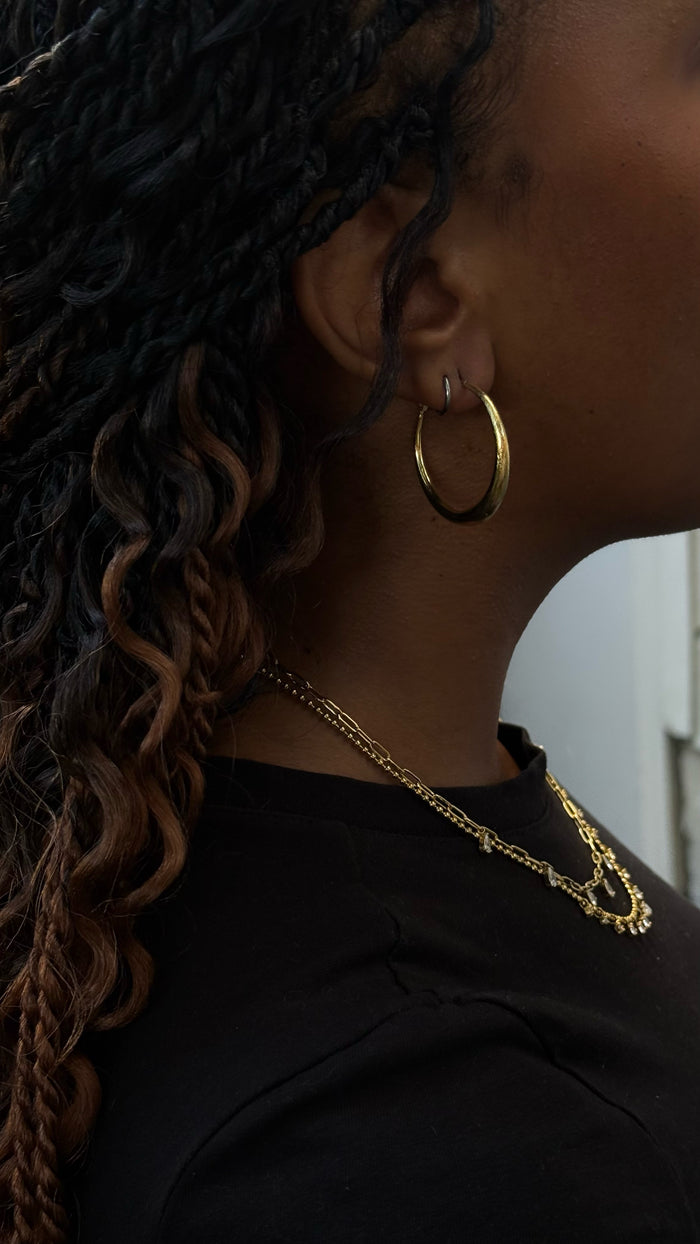 Close up of a woman in a black shirt wearing gold hoops and necklaces.