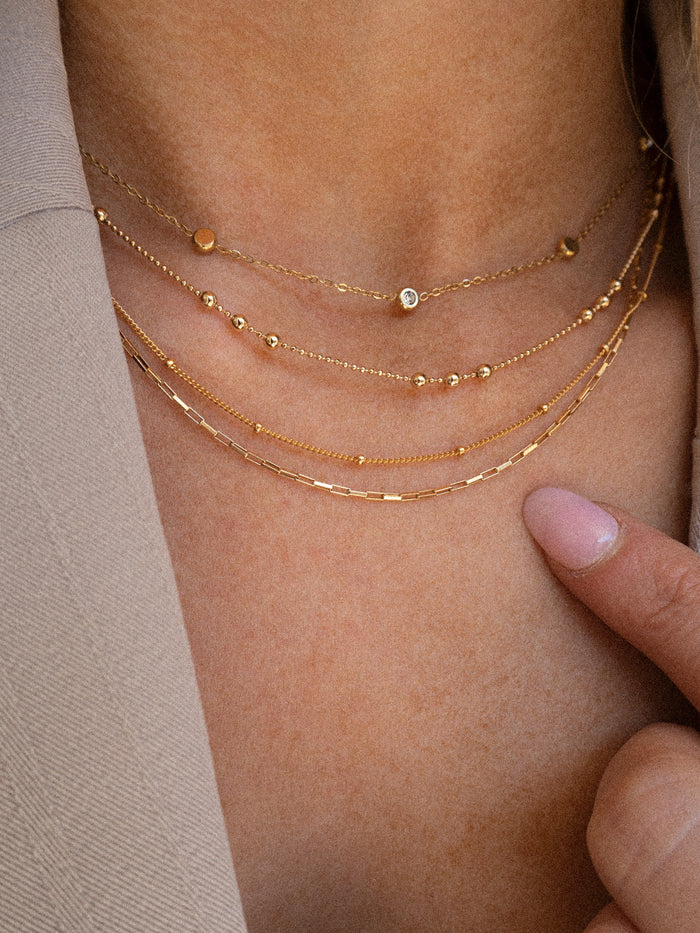 Model wearing the gold Joy square link necklace layered with dainty chains