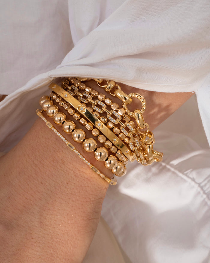 Close up of a person's wrist with a white long sleeve shirt and assorted gold bracelets