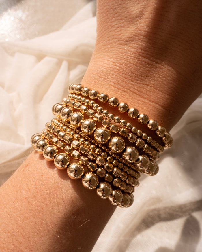 Close up of a wrist with assorted gold bead bracelets on a white background