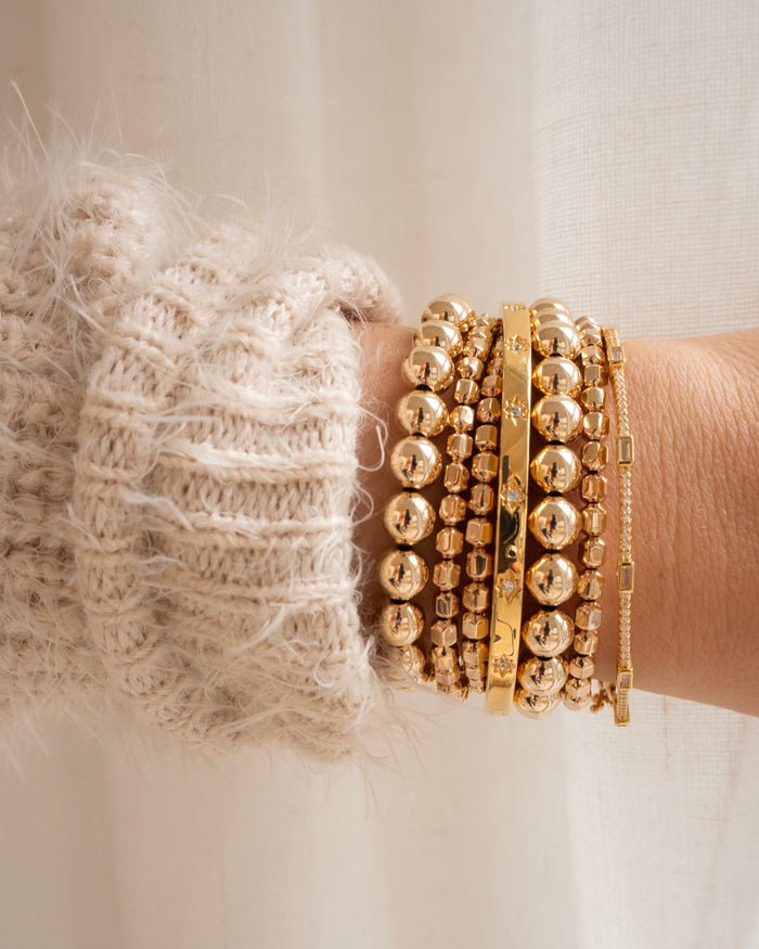 Close up of a person's wrist in a white sweater, with assorted gold bracelets