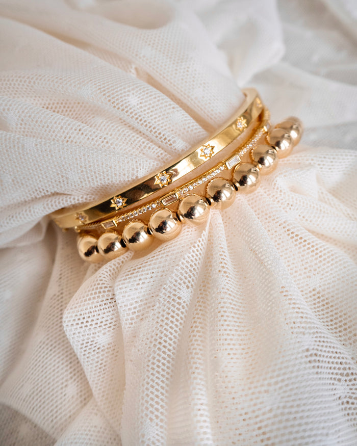 Three gold bracelets on a white tulle background