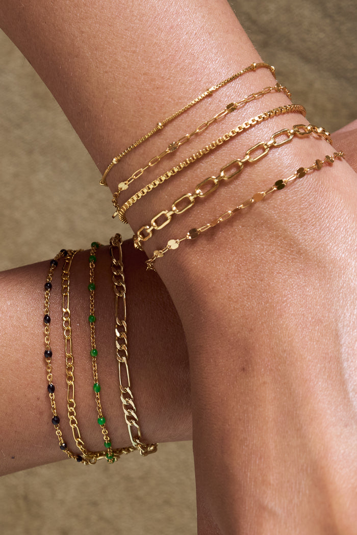 Close up of two wrists with dainty gold chain bracelets on a tan background