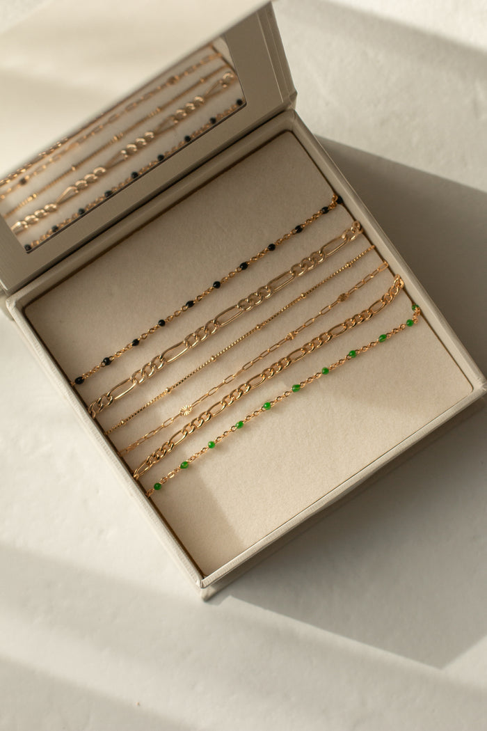 Dainty gold bracelets laid out in a beige jewelry box against a white background