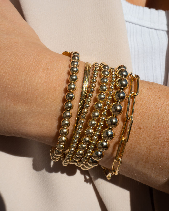 Close up of a person in a beige blazer wearing gold bracelets