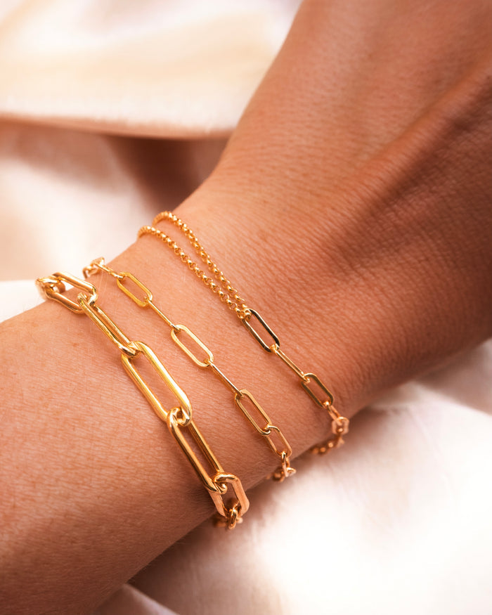 Close up of a wrist with gold link bracelets on a pink background