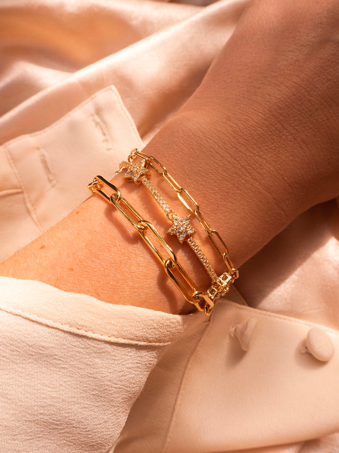 Close up of a wrist with gold and stone bracelets on a cream fabric background