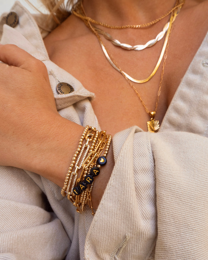 A person wearing an oversized beige shirt and assorted gold jewelry