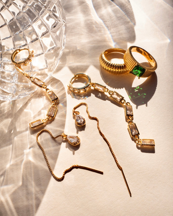 Various gold and stone earrings and rings on a neutral surface