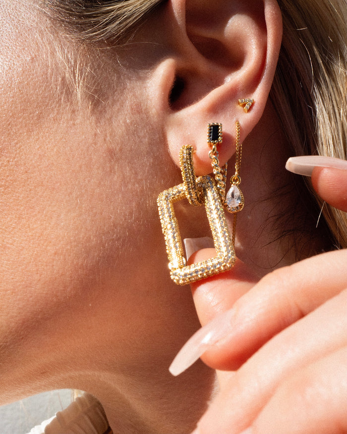 Close-up of an ear with multiple gold and crystal earrings