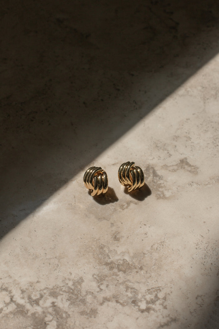 Gold earrings on a neutral stone background