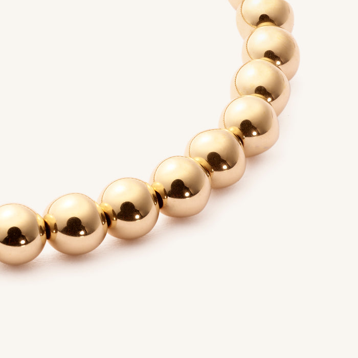 Close up of a gold bead bracelet on a white background