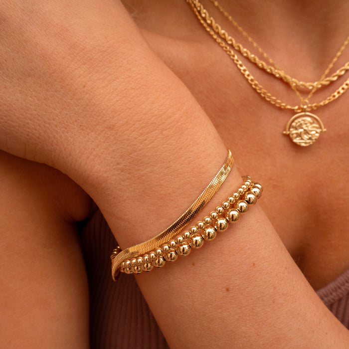 Close up of a person's chest and wrist wearing a pink tube top and assorted gold jewelry
