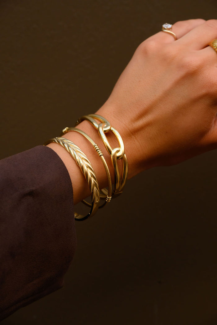 A wrist with a brown sleeve and gold cuff bracelets