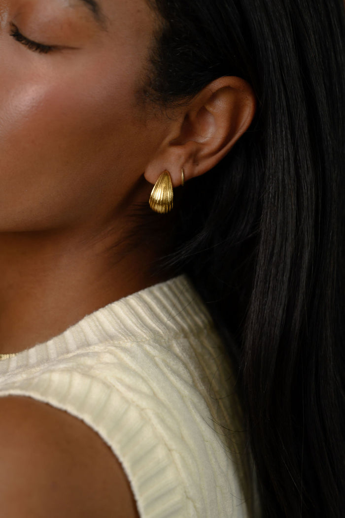 A woman wearing gold earrings and a white top