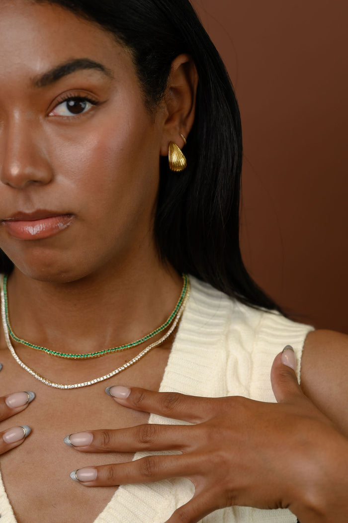 A woman wearing gold earrings and stone necklaces against a brown background