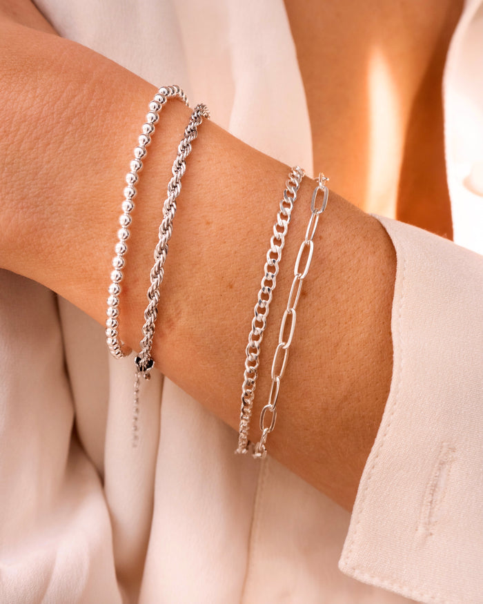 Close up of a person's wrist and chest wearing a white long sleeve top and silver bracelets