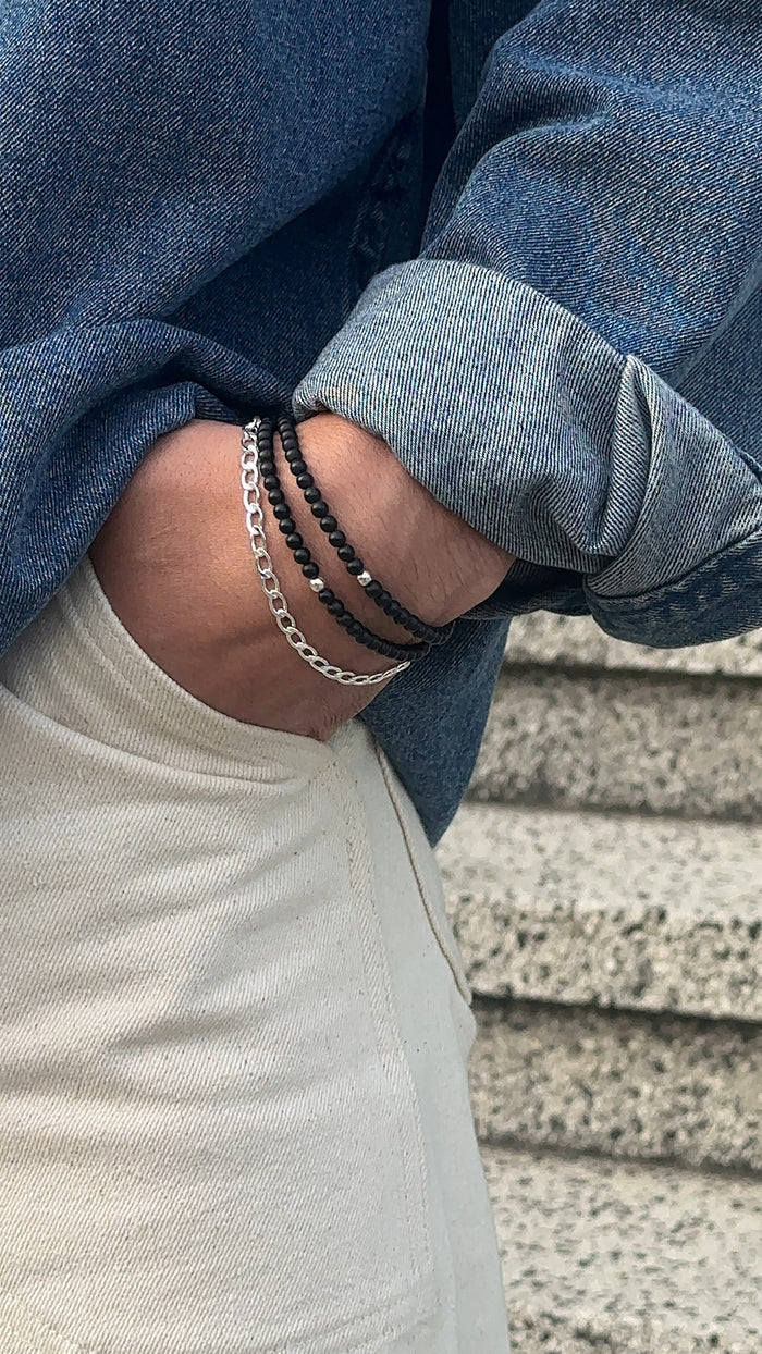 A man wearing a blue shirt, white pants, and a silver and black bracelets