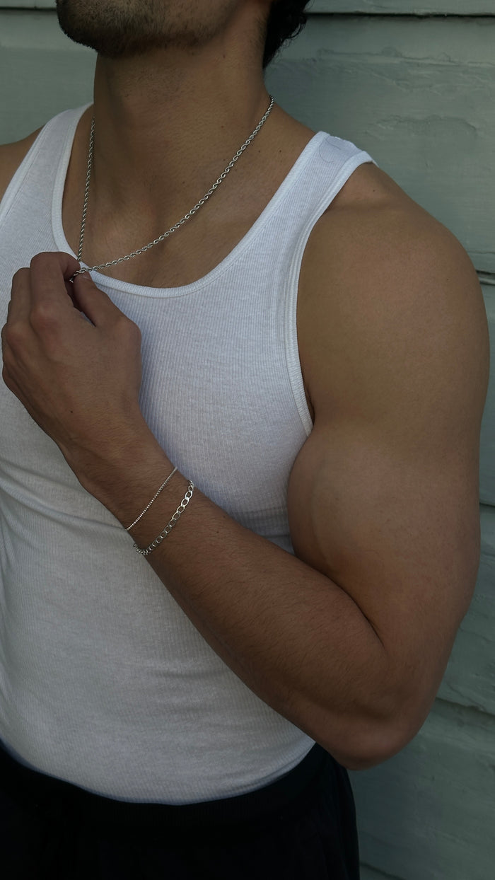 Close up of a man wearing a white tank top and various silver jewelry